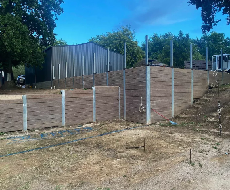 Malibu Woodgrain Concrete Sleepers in Jasper Brown Being Installed on Large Retaining Wall and Supplied by Sunset Sleepers