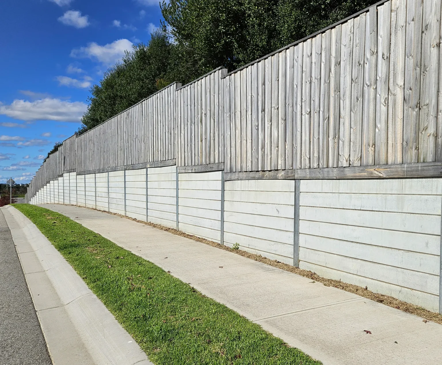 Plain Grey Smooth Concrete Sleepers in The Marina Range used as an Under Timber Fence Retaining Wall Project and Supplied by Sunset Sleepers